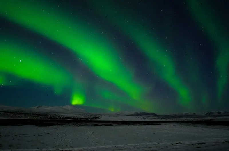 Green curtains of the northern lights over a dark snowy landscape